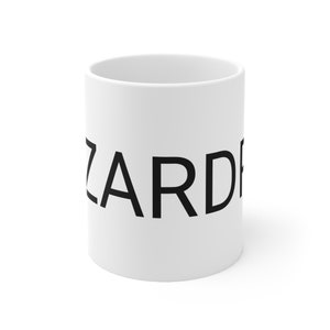 May include: A white ceramic mug with the word 'ZARD' printed in bold, uppercase, black sans-serif font. The mug is cylindrical and has a simple design. The text is centered on the mug, and the mug is shown against a white background.