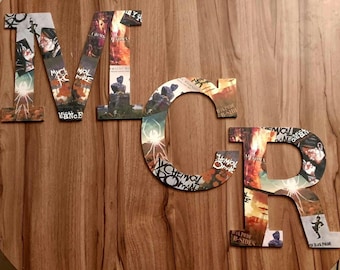 May include: Wooden letters spelling "MCR" are displayed on a wooden surface. The letters are decorated with album art and images. The letter "M" has a spider graphic. The letter "C" has a spider graphic. The letter "R" has a silhouette of a person.