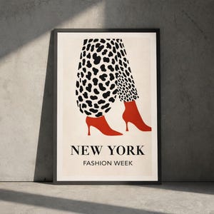 Pode incluir: Uma impressão artística emoldurada com uma ilustração de moda. A obra retrata um par de pernas com saltos vermelhos e calças com estampa de manchas pretas e brancas. As palavras "NEW YORK FASHION WEEK" são impressas abaixo.