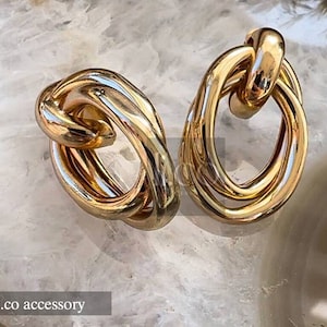May include: A pair of gold-toned hoop earrings with a knotted design. The earrings are made of thick metal and have a polished finish.