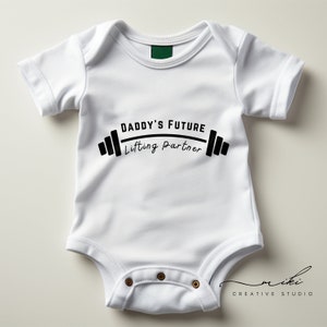 Peut inclure: Combinaison blanche pour bébé avec un texte noir qui dit "Daddy's Future Lifting Partner" avec un graphique de barre d'haltères noir.