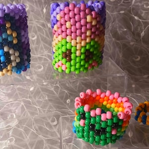 May include: Four colorful beaded bracelets. One is purple, blue, and white. Another is pink, green, and brown. A third is orange, pink, and green. The last is blue and yellow. These handmade bracelets are perfect for adding a pop of color to any outfit.