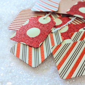 May include: A collection of decorative gift tags with various patterns. Some tags feature red glitter with white polka dots, while others have red and black stripes. The tags are strung with white twine, suggesting they are ready for use.