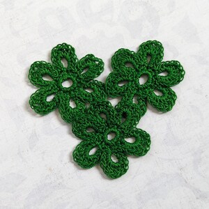 May include: Three green crocheted flowers with a delicate, lacy design.
