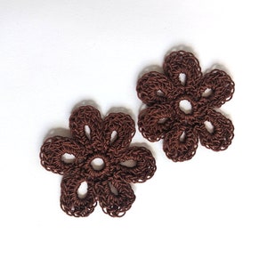 May include: Two brown crocheted flower shapes. The flowers have five petals each and are made with a delicate, openwork stitch.