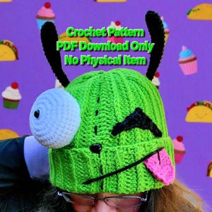 Puede incluir: Un gorro verde tejido a ganchillo con un diseño de cara de monstruo, con un ojo blanco grande, cejas negras, una nariz negra y una lengua rosa. El gorro tiene características negras en forma de antena. El texto en la imagen dice "Crochet Pattern PDF Download Only No Physical Item."