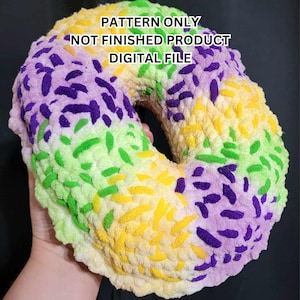 May include: A crochet pattern for a donut shaped plush toy. The donut is made in a multi-colored ombre pattern of purple, green, and yellow. The text on the image reads "PATTERN ONLY NOT FINISHED PRODUCT DIGITAL FILE".