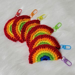 May include: A collection of handmade crochet rainbow keychains. Each keychain features a vibrant rainbow design with red, orange, yellow, green, blue, and purple colors. The keychains have colorful metal clasps for easy attachment.