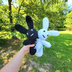 May include: Two crocheted plush bunny toys, one black and one white, with stitched-on eyes and X marks for mouths. The toys are held together by a hand.