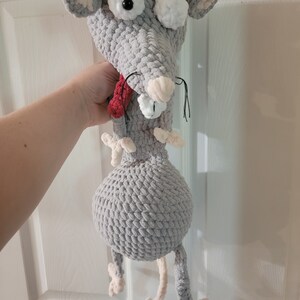 May include: A gray crocheted rat plush toy with large white eyes and a red scarf. The rat has a long tail and is standing on its hind legs.
