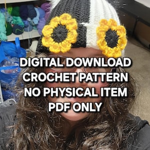 Puede incluir: Un gorro de ganchillo en blanco y negro con dos acentos de girasol amarillos y un pomp&oacute;n blanco. El texto de la imagen dice: DESCARGA DIGITAL PATR&Oacute;N DE GANCHILLO SIN ART&Iacute;CULO F&Iacute;SICO SOLO PDF.