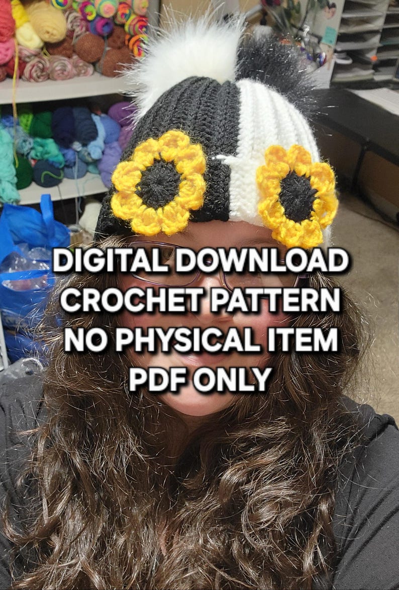 Puede incluir: Un gorro de ganchillo en blanco y negro con dos acentos de girasol amarillos y un pomp&oacute;n blanco. El texto de la imagen dice: DESCARGA DIGITAL PATR&Oacute;N DE GANCHILLO SIN ART&Iacute;CULO F&Iacute;SICO SOLO PDF.