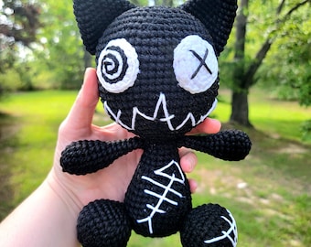 May include: Black crocheted cat plush toy with white embroidered eyes, a stitched-on mouth, and a fishbone design on its back.