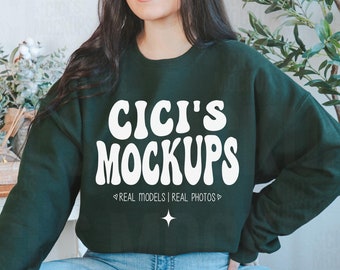 May include: A dark green sweatshirt with the text "CICI'S MOCKUPS" in white, with the tagline "REAL MODELS | REAL PHOTOS" below. The sweatshirt is being worn by a person with long dark hair.