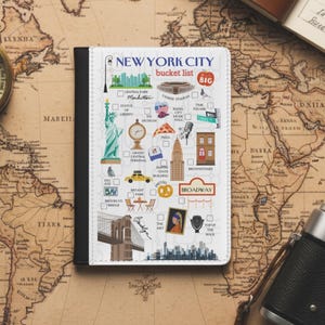 Könnte beinhalten: Ein New York City Bucket List-Journal mit schwarzem Einband, das Illustrationen berühmter Wahrzeichen wie der Freiheitsstatue und der Brooklyn Bridge zeigt. Das Journal enthält Kontrollkästchen für jeden Ort.