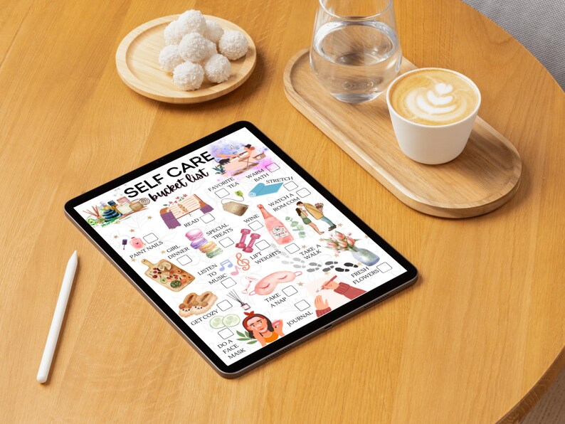 May include: A digital tablet displaying a self-care bucket list with illustrations of various activities, including reading, taking a bath, listening to music, and getting a manicure. The list is on a wooden table with a cup of coffee and a glass of water.