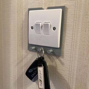 Peut inclure: Un interrupteur double blanc avec un porte-clés gris. Deux clés sont suspendues au porte-clés. Un porte-clés porte le logo Jaguar, l'autre une étiquette blanche avec un motif.