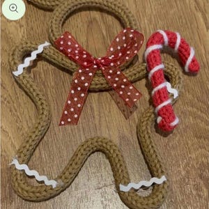 May include: Handmade crochet Christmas decorations. The set includes a gingerbread man, a candy cane, and a wreath. The gingerbread man has white trim and a red polka dot bow. The candy cane is red and white. The ornaments are brown, red, and white.