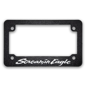 May include: Black license plate frame with the words "Screamin Eagle" in white script. The frame has a textured surface and four mounting holes.