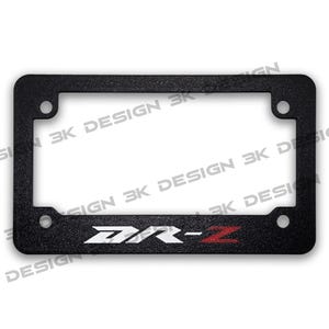 May include: Black license plate frame with the text "DR-Z" in white and red. The frame has a textured surface and mounting holes in each corner. The words "3K DESIGN" are printed around the frame.