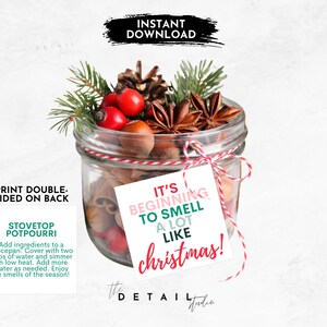 May include: A glass jar filled with cinnamon sticks, star anise, and other spices. A white tag with the text "It's beginning to smell a lot like Christmas!" is attached to the jar.