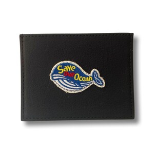 May include: Black leather wallet with a blue whale embroidered patch that says "Save Our Ocean" in yellow, red, and white lettering.