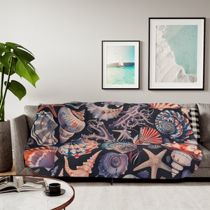 May include: A navy blue throw blanket with a colorful seashell pattern. The blanket features a variety of seashells, including conch shells, scallop shells, and starfish. The blanket is perfect for adding a touch of coastal charm to any room.