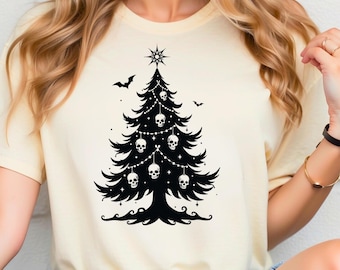 May include: Cream-colored t-shirt featuring a black graphic of a Christmas tree decorated with skulls and string lights. A star tops the tree, with bats flying nearby. The design is a unique blend of holiday and gothic themes.