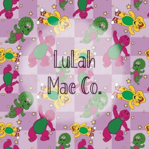May include: A repeating pattern featuring cartoon dinosaurs in shades of purple, green, and yellow, with a light purple checkered background and scattered yellow stars. The text "Lulah Mae Co." is overlaid on the design.