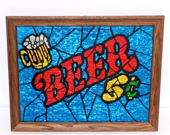May include: A framed stained glass panel with the word "BEER" in red, outlined in black. A yellow beer mug and a "5¢" sign are also featured. The background is blue with a stained glass effect, and the frame is brown.