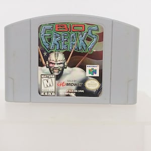 May include: A gray Nintendo 64 game cartridge for "Bio Freaks." The label features the game's title in a green and blue design, a character illustration, and the ESRB rating "M" for Mature. The cartridge is a standard size.