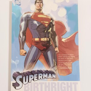 May include: A Superman comic book titled "Birthright: The Origin of the Man of Steel." The cover features a muscular Superman in a red cape and blue suit, with the Superman logo on his chest. The background is a blue sky.