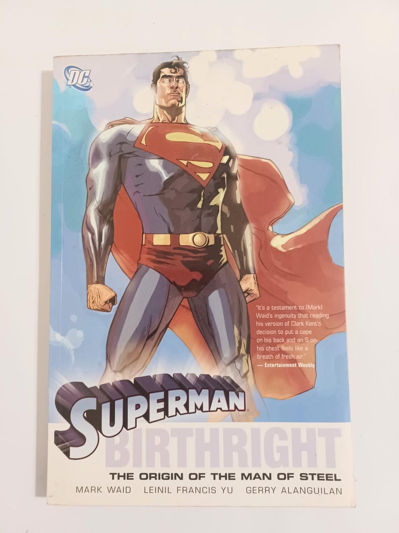 May include: A Superman comic book titled "Birthright: The Origin of the Man of Steel." The cover features a muscular Superman in a red cape and blue suit, with the Superman logo on his chest. The background is a blue sky.