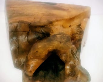 May include: A handcrafted wooden sculpture with a natural, organic form. The sculpture features a mix of light and dark brown tones, with a smooth, polished surface and a rough, textured base. The design includes a dark, cave-like opening.