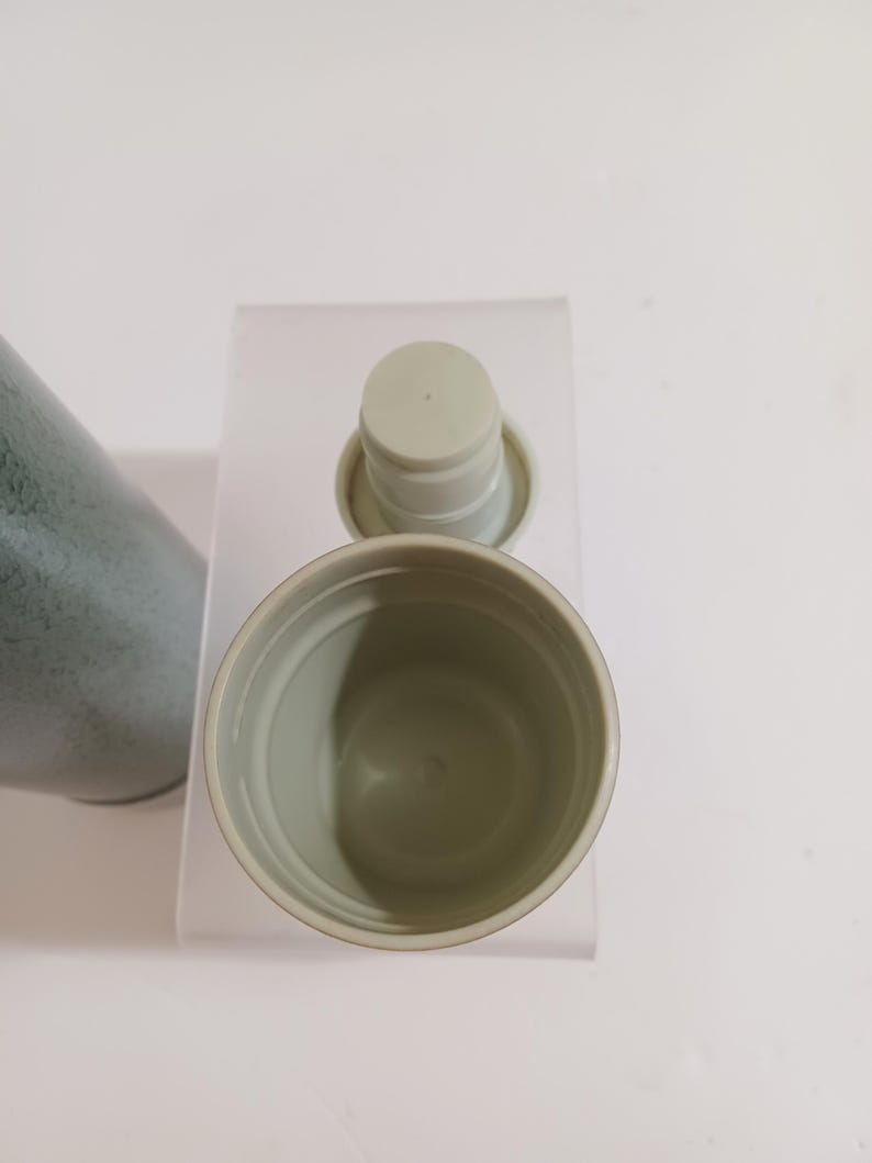 May include: An overhead view of a light green travel mug with a matching lid. The mug is open, revealing the interior. The lid is detached and placed next to the mug. The mug has a textured exterior and is set against a white background.