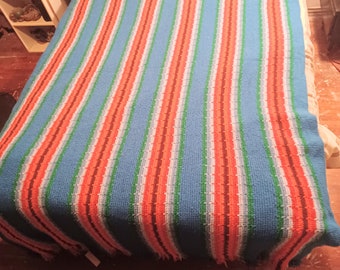 May include: A striped crocheted throw blanket with blue, green, orange, and white stripes. The blanket has a fringe border.