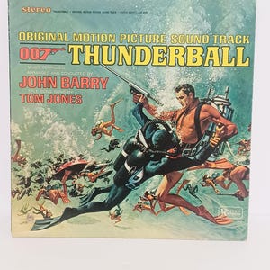 May include: Vintage vinyl record album cover for the James Bond film "Thunderball." The cover features a colorful illustration of divers in a water scene, with the title and artist names prominently displayed. The album is a stereo recording.