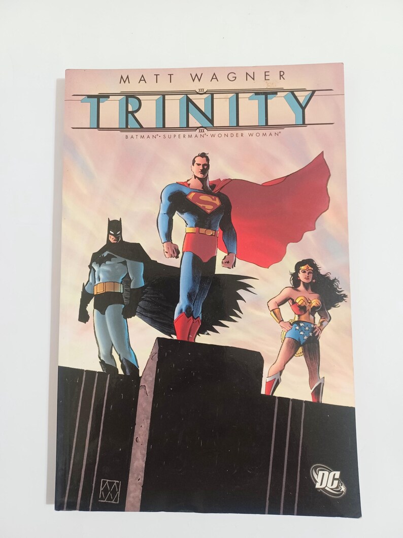 May include: A comic book titled "Trinity" by Matt Wagner, featuring Batman, Superman, and Wonder Woman. The cover art depicts the three superheroes standing together against a colorful sky. The DC Comics logo is visible.