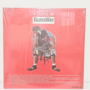 May include: A red album cover with the text "A Taste of Bluesway" and "Bluesway." The cover features a seated figure in colorful clothing. Text on the cover describes the album's contents and the artists featured.