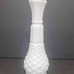 May include: A white milk glass vase featuring a textured diamond pattern on the lower bulbous section, a vertical ribbed neck, and a scalloped rim. A small wooden square tile with the letter A and the subscript 1 is placed at the base.