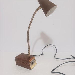 May include: A vintage desk lamp with a brown conical shade and a flexible, brass-colored neck. The base is a rectangular block of wood-grain material. The lamp has a black power cord and a small label that reads "benson".
