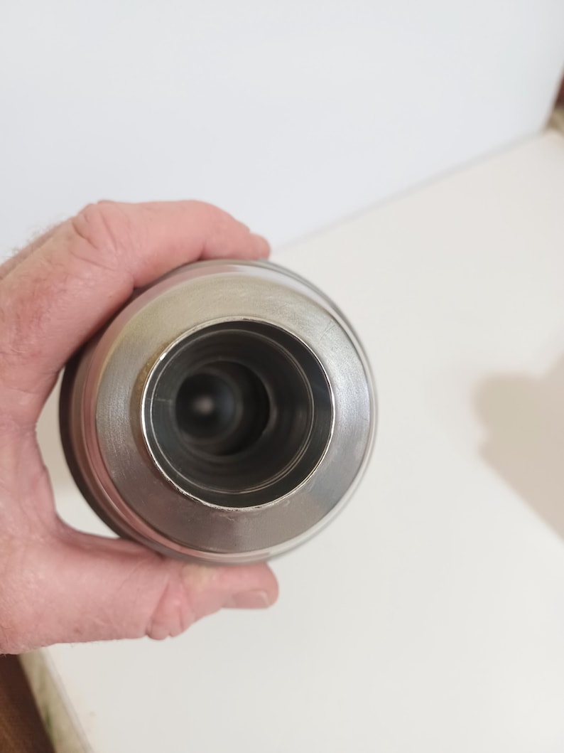 May include: A stainless steel insulated tumbler with a wide mouth and a silver finish. The tumbler has a cylindrical body and a rounded top, designed to keep beverages hot or cold. The interior is dark, suggesting insulation.