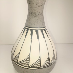 May include: A decorative ceramic vase with a gray speckled neck and base. The body of the vase is off-white with a black geometric design. The vase has a rounded bottom and a flared neck.