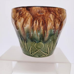 May include: A handcrafted ceramic bowl with a unique design. The bowl features a gradient of colors, transitioning from a dark brown rim to a green base. The exterior is decorated with carved patterns, adding texture and visual interest. The bowl is a decorative piece.
