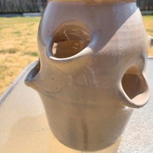 May include: A light beige glazed ceramic strawberry planter featuring a wide top opening and multiple protruding side pockets for planting. The vessel has a smooth, glossy finish with a rounded body shape and a sturdy base, designed for vertical gardening.