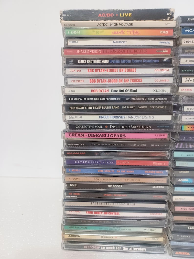 May include: A vertical stack of numerous music compact discs in plastic jewel cases. The spines are visible, displaying various artist names and album titles including AC/DC, Bob Dylan, Bob Seger, Bruce Hornsby, Cream, and Everclear in various colors.