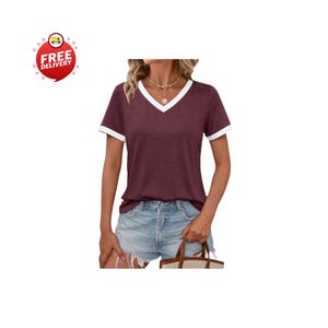 May include: A burgundy V-neck t-shirt with white trim on the collar and sleeves. The short-sleeved top is paired with denim shorts. A red circle with the words "FREE DELIVERY" is in the upper left corner.