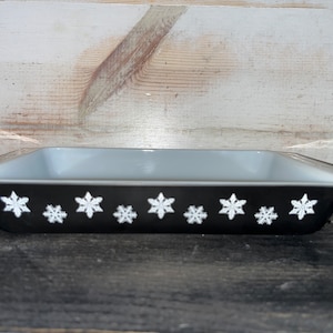 May include: A black baking dish with a light gray interior and a white snowflake design around the rim.