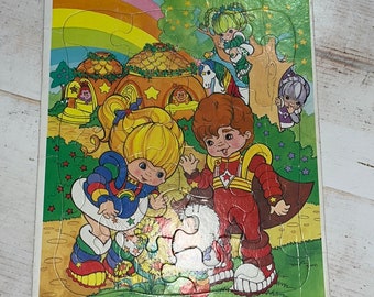 Puede incluir: Un rompecabezas vintage Rainbow Brite Frame Tray con una ilustración colorida de Rainbow Brite y sus amigos. El rompecabezas está hecho de cartón y tiene un acabado brillante. El rompecabezas está en buen estado y está listo para ser disfrutado.