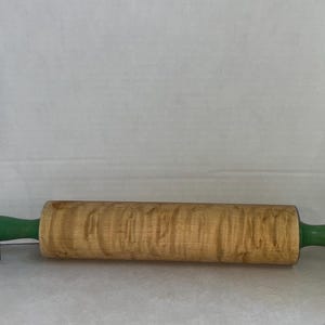 Puede incluir: Tres herramientas de cocina vintage con mangos verdes. Un rodillo de madera con acabado de madera natural, un machacador de patatas con marco de metal y un mazo de madera.